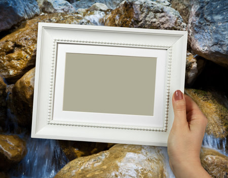 Wooden frame in beautiful woman hands on the background Waterfall in the early morning.
