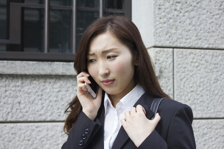 Unhappy young business woman talking with a mobile phoneの写真素材