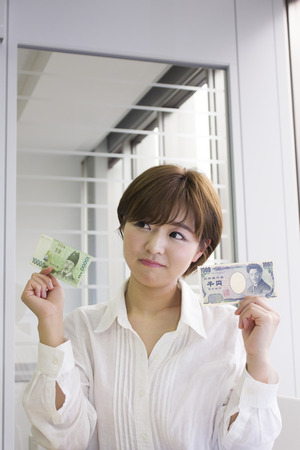 Unhappy young woman holding Japanese Yen and Korean Wonの写真素材