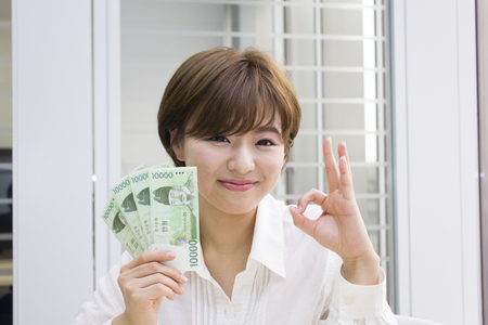 Young woman holding Korean Won with OK signの写真素材