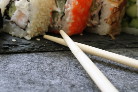 Rolls with shrimp, sesame, tuna, bacon, cheese, cucumber, vegetables and sushi sticks on a black board. Close-up.の写真素材