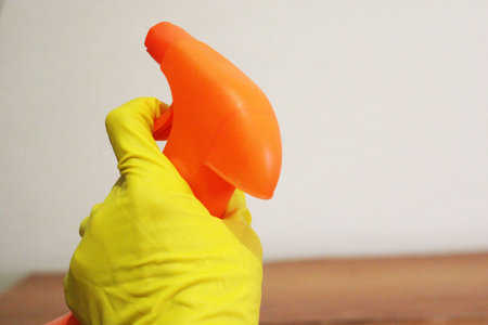 Image of a hand wearing a rubber glove with a cleaning spray.