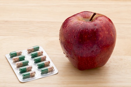 Green capsules bliter pack and fresh red apple on wooden backgroundの写真素材