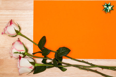 Blank orange page with white rose on a wooden background. Copy space.Top view