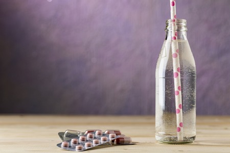 A bottle of water with a straw and blister pack tablets on wooden tableの写真素材