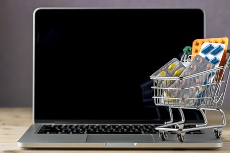 Mini shopping cart with pill blister pack on open laptop.Concept forn online storeの写真素材