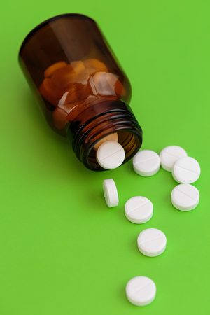 Glass bottle and pile of white pills on green backgroundの写真素材