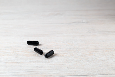 Three black medicine capsules on bright tableの写真素材