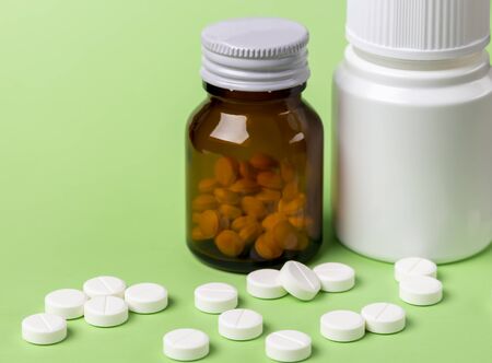 Two glass bottles of pills. Scattered white round tablets next to each other. Green flat background.の写真素材