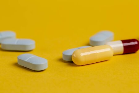 A variety of blue, yellow and red pills and capsules against a yellow background.の写真素材