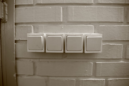 Four white household electric switches on a brick wall