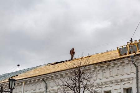 A man on the roof is carrying out repairs with wooden boardsの写真素材