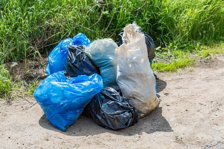 Blue, white and black polyethylene bags with garbage lie on a dirt roadの写真素材