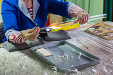 Glassblower woman works with a gas burner and a fragile glass billetの写真素材
