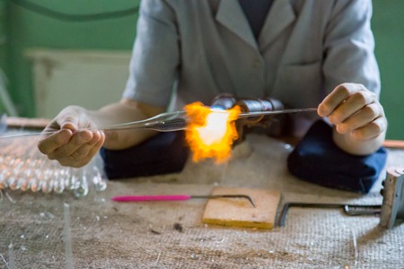 Glassblower woman works with a gas burner and a fragile glass billetの写真素材