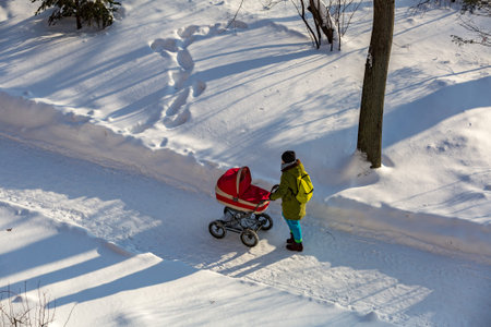 Woman with a baby stroller walks through the winter park in the frost