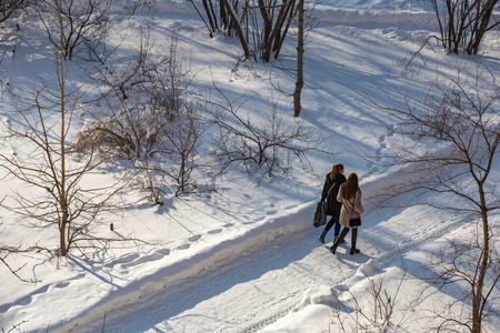 Two fashion girls are walking through the snow-covered park in a frosty winterの写真素材