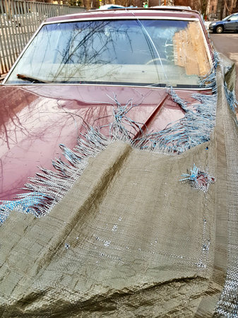 Abandoned rotting car under a torn canvas cover on the street
