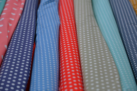 Bright multi-colored fabrics in rolls lie in a row on the counter of the oriental market