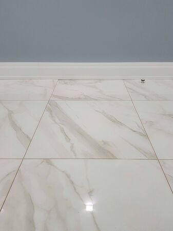Marble floor. Square glossy tile with patterns, part of the wall and plastic baseboardの写真素材