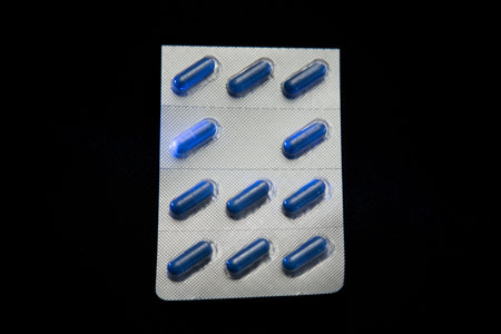 Blue oval medical capsules in silver plastic packaging on a black background