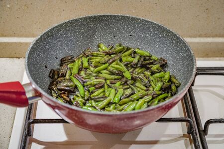 Fresh juicy green french beans are fried in a frying pan on a kitchen gas stoveの写真素材