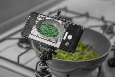 Fresh juicy green french beans are fried in a frying pan on a kitchen gas stoveの写真素材