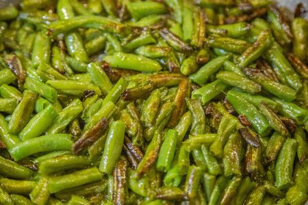 Fresh juicy green french beans are fried in a frying pan on a kitchen gas stoveの写真素材