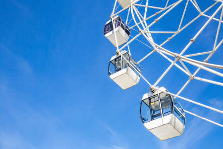 Big ferris wheel with white cabins in an amusement park against a blue sky during the sunny dayの写真素材