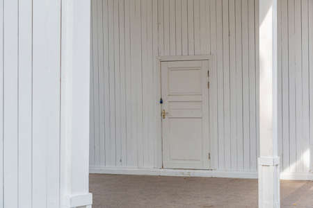 Part of the wall of a white board building with a closed doorの写真素材