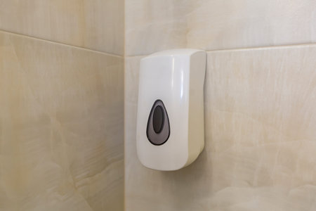 White plastic liquid soap dispenser on tiled bathroom wall