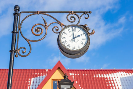 Round glass clock with black arrows on a city streetの写真素材