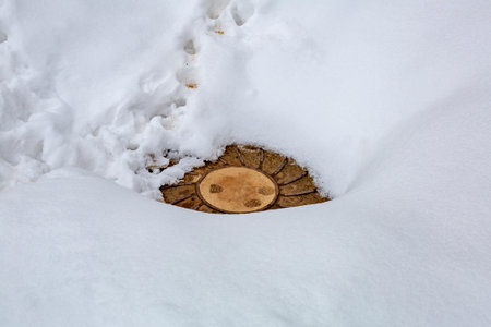 Old iron sewer manhole is covered with snow on a winter dayの写真素材