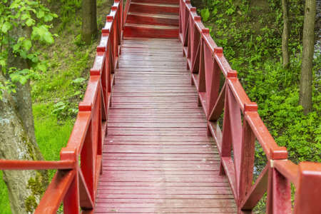A small bridge made of wooden boards with handrails across a narrow stream in a city parkの写真素材