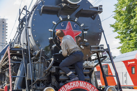 Moscow, Russia - July 11, 2021: Worker washes a black retro steam locomotive on the railway platform...