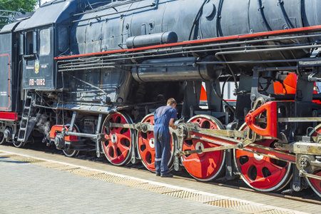 Moscow, Russia - July 11, 2021: Worker inspects a black retro steam locomotive on the railway platform of the Rizhsky stationのeditorial素材