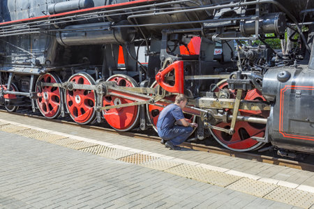 Moscow, Russia - July 11, 2021: Worker inspects a black retro steam locomotive on the railway platform of the Rizhsky stationのeditorial素材
