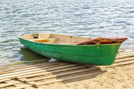 Empty shabby plastic boat for river walks stands on the shore of the pondの写真素材
