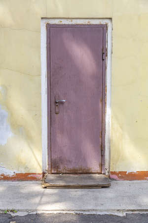 Part of the yellow stone wall of an old building and a closed rusty doorの写真素材