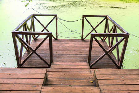 A small wooden pier for boats at the abandoned city pond with duckweedの写真素材