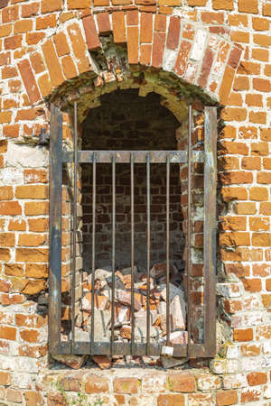 The ruined entrance to the ancient brick tower is closed with an iron gratingの写真素材