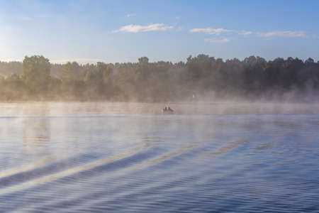 Clouds of thick fresh fog over the calm water surface of the riverの写真素材