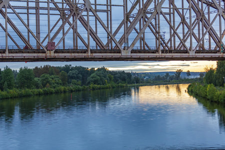 Railway transport bridge made of steel piles and beams across the river during sunsetの写真素材
