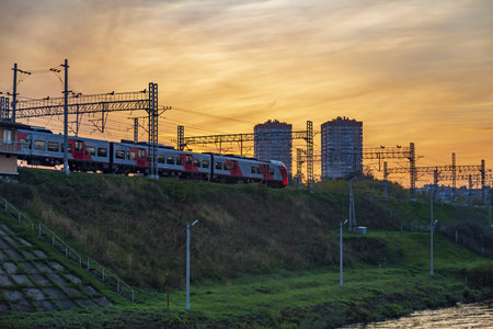 Moscow, Russia - September 12, 2021: The high-speed electric train Lastochka of Russian Railways moves along a rampart against the backdrop of a picturesque sunsetのeditorial素材
