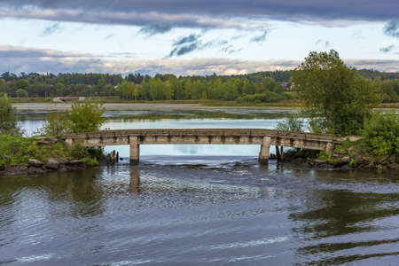 Old weathered pedestrian stone bridge over a narrow river in a rural woodland areaの写真素材