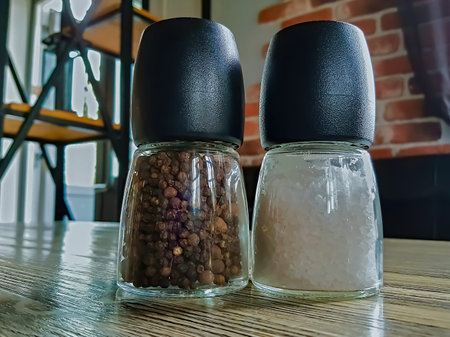 Large salt shaker made of glass and black plastic on a wooden table in a cafe