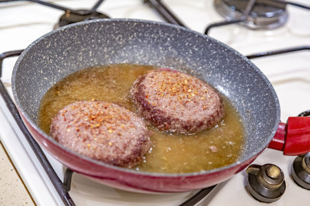 Juicy minced beef patties are fried in oil in a frying pan on a gas stoveの写真素材