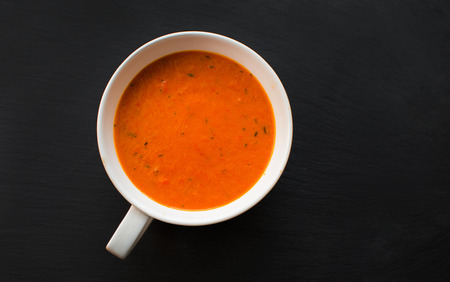 Cream soup with roasted peppers and tomatoes on black plate, top viewの写真素材