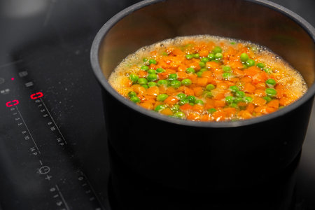 peas and carrots are cooked in a pot on an induction hob