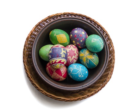 colorful painted Easter eggs in a woven straw basket isolated on white backgroundの写真素材